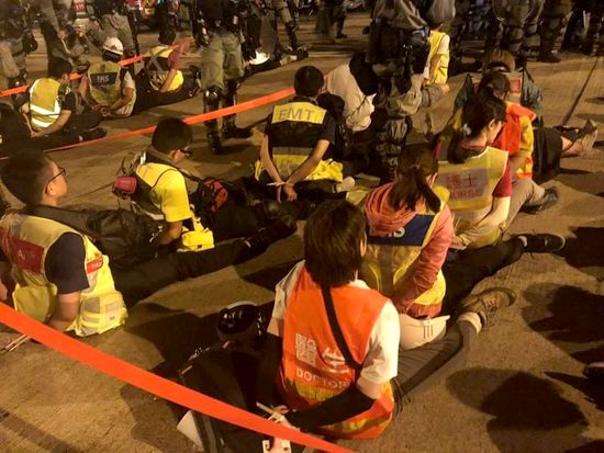 의료진을 나타내는 표시가 적힌 조끼를 입은 사람들이 홍콩 경찰에게 체포돼 뒤로 손을 묶인채 길바닥에 앉아 있다. 이미지 출처: Copyright &copy; 2019 Darren Mann